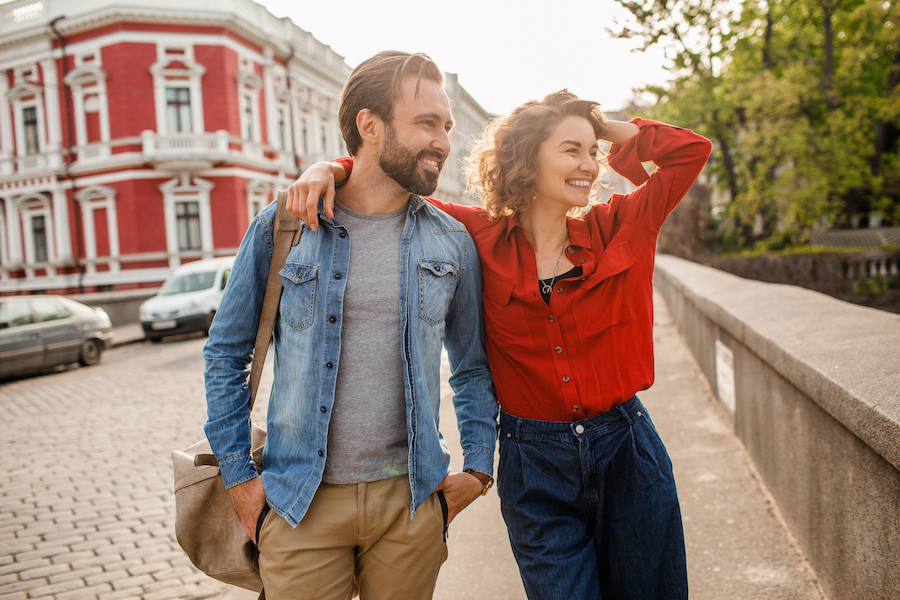 attractive happy smiling man and woman traveling together in Europe, stylish couple in love walking in street on romantic trip, sunny summer city, having fun