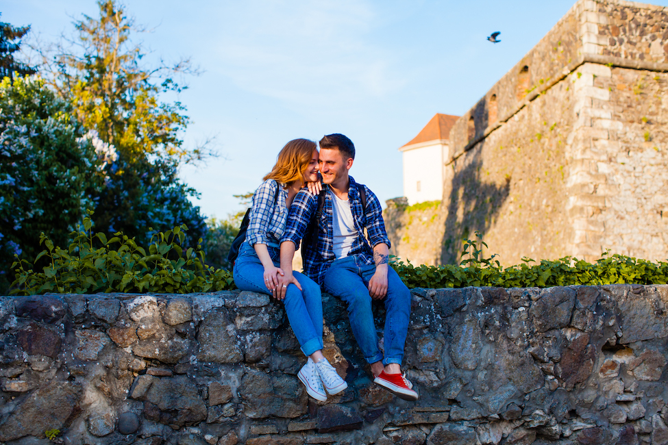 Young romantic couple sitting embracing on a wall near the Uzhhorod castle. Historical places of interest in old cities concept